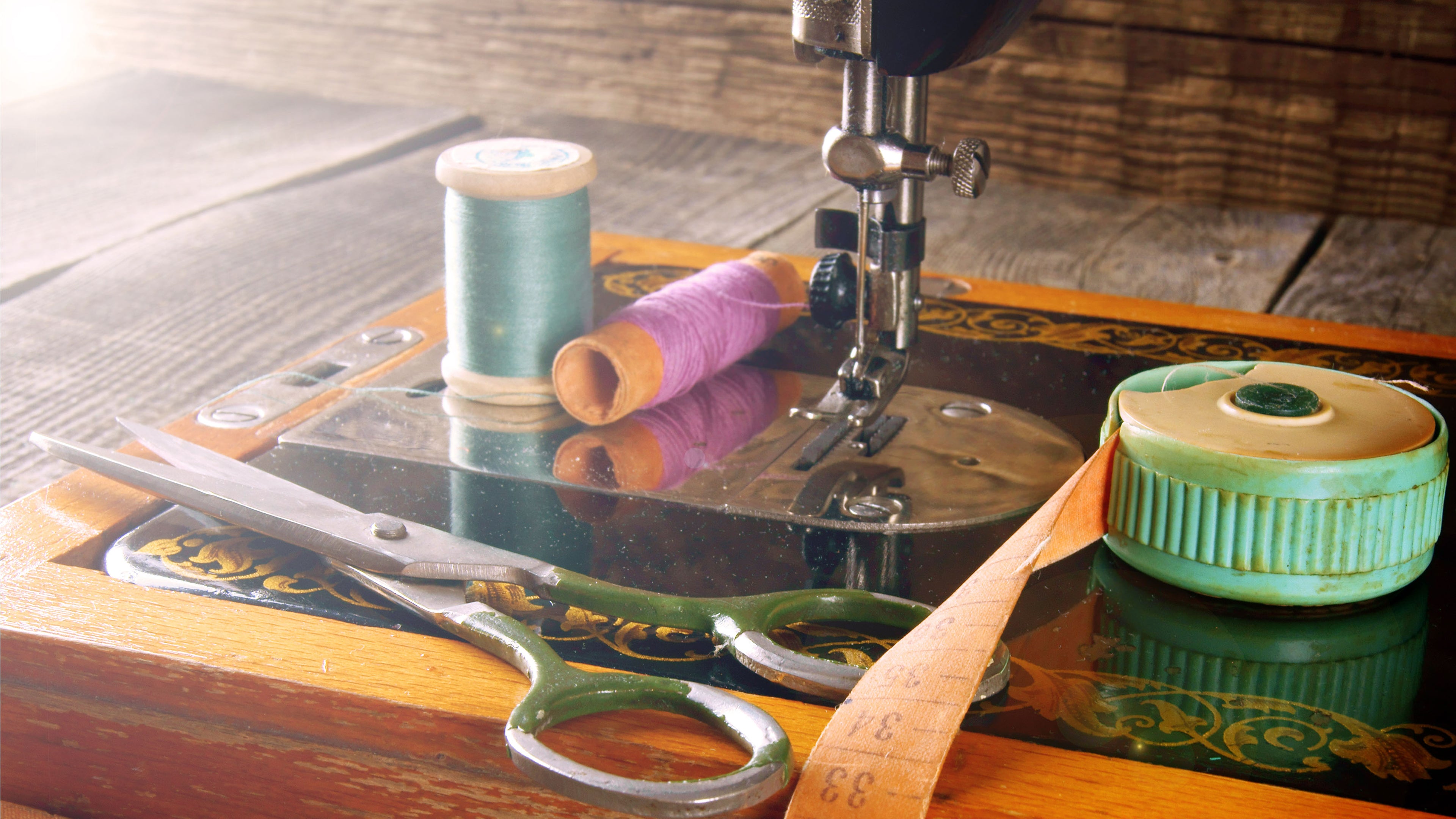 Sewing machine with spools of thread, scissors, and measuring tape on a wooden surface.